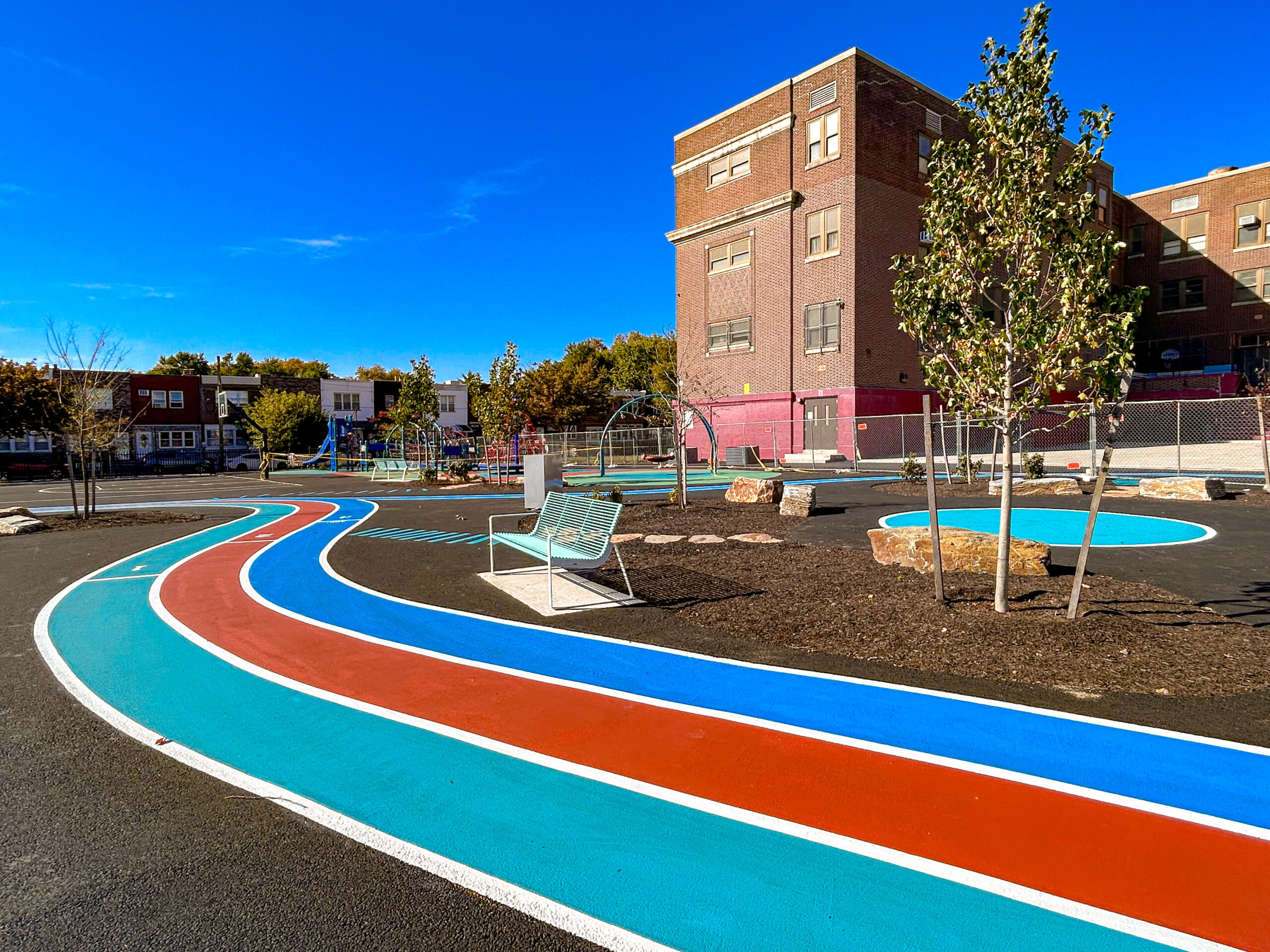 Curved blue, red, and teal running track with bench seating and trees outside Bregy Elementary School